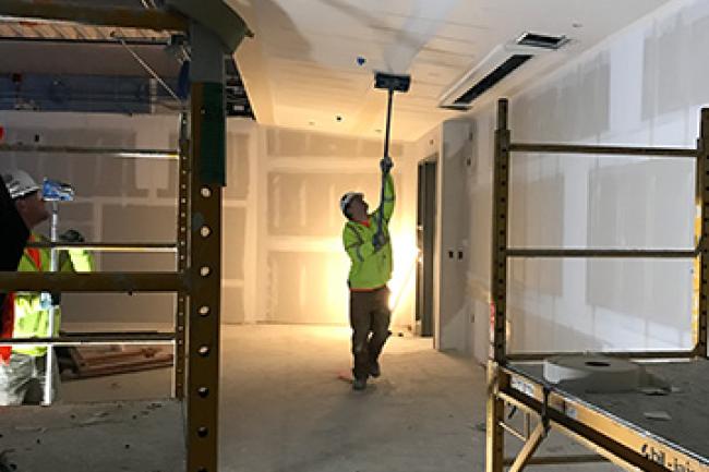 Worker paints ceiling with a roller in a space under construction