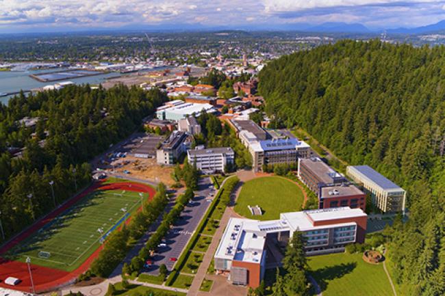 Aerial view of WWU campus, surrounded by trees, mountains, and water, with Kaiser Borsari Hall rendered in